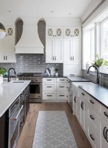 White shaker style kitchen cabinets with black hardware and gray subway tile backsplash in a modern kitchen