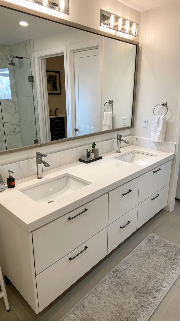 Modern white bathroom cabinets with double undermount sinks, quartz countertop, chrome faucets, and large wall mirror in a contemporary bathroom