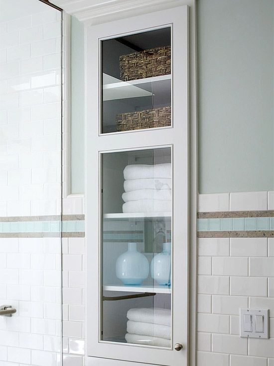Tall white bathroom cabinet with framed glass door showcasing towels and decor
