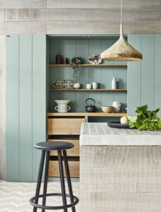 Kitchens and Bathrooms: minimalist sage-green pantry nook with open wood shelves, handmade-tile island, rustic pendant light, and black bar stool.