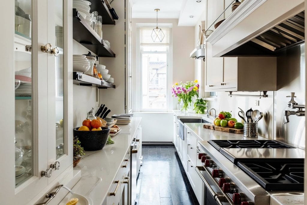 Bright white galley kitchen cabinets with glass fronts, stainless steel appliances, open shelving, and natural light creating a modern corridor layout