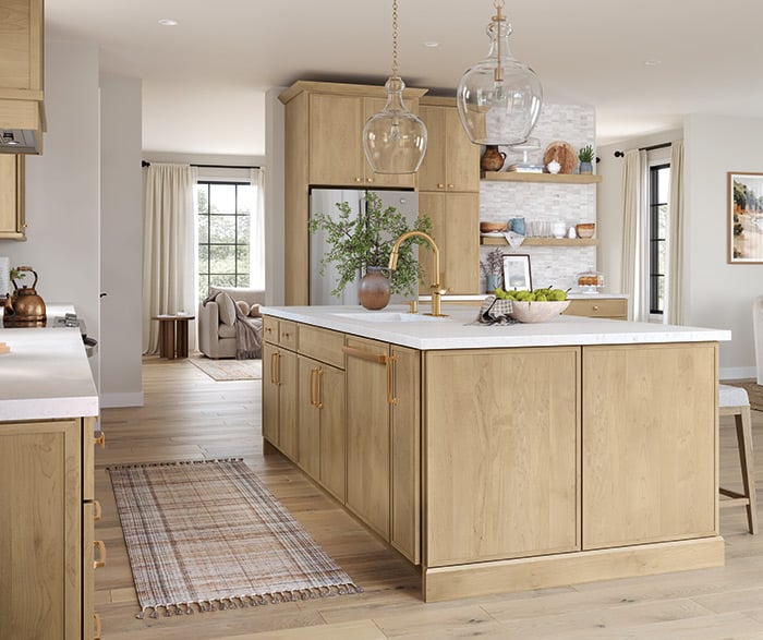 Kitchen and Bathroom Cabinets – natural oak flat-panel kitchen with large quartz island, brass hardware and faucet, globe pendants, open shelves, and wide-plank floor in bright natural light.