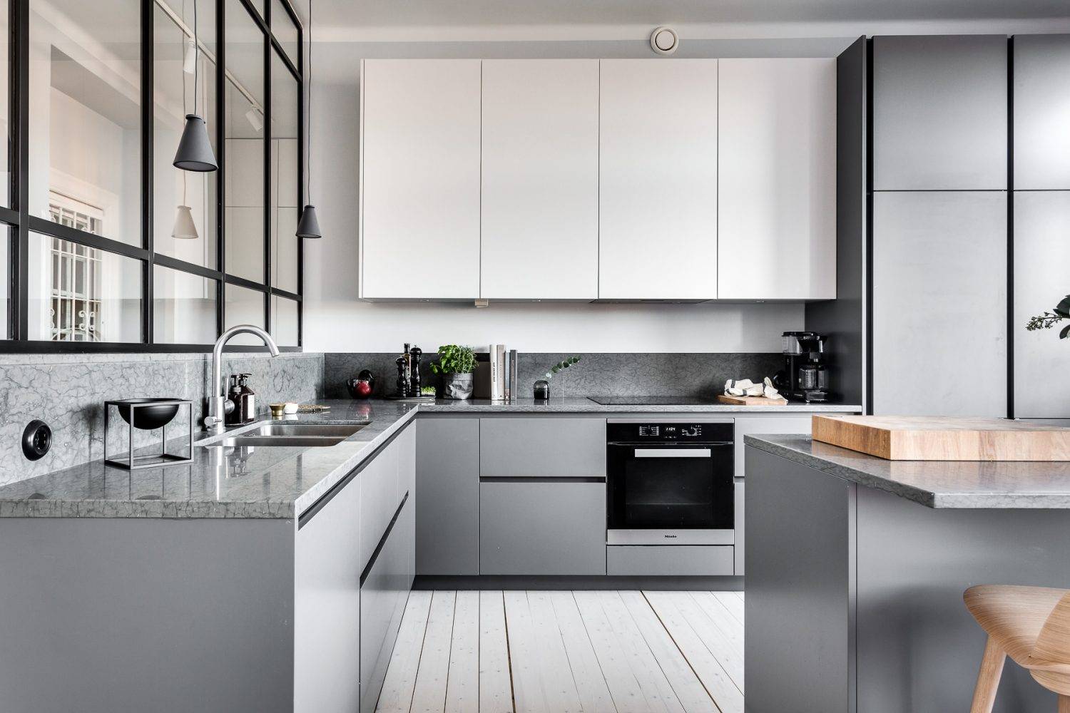 Kitchen and Bathroom Cabinets in a sleek modern kitchen—matte gray flat-panel bases, white uppers, gray stone countertop/backsplash, black-framed glass partition, and compact island.
