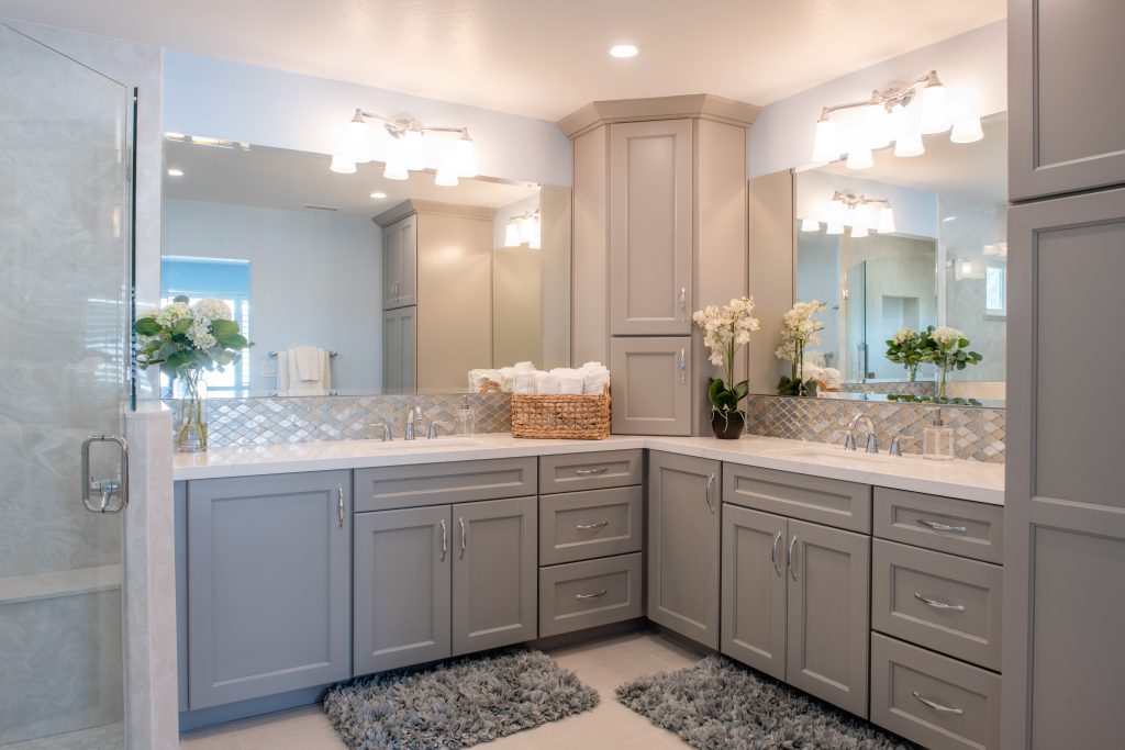 Bathroom Cabinets – gray shaker L-shaped double vanity with center tower, quartz countertop, mosaic backsplash, dual sinks, and glass shower.