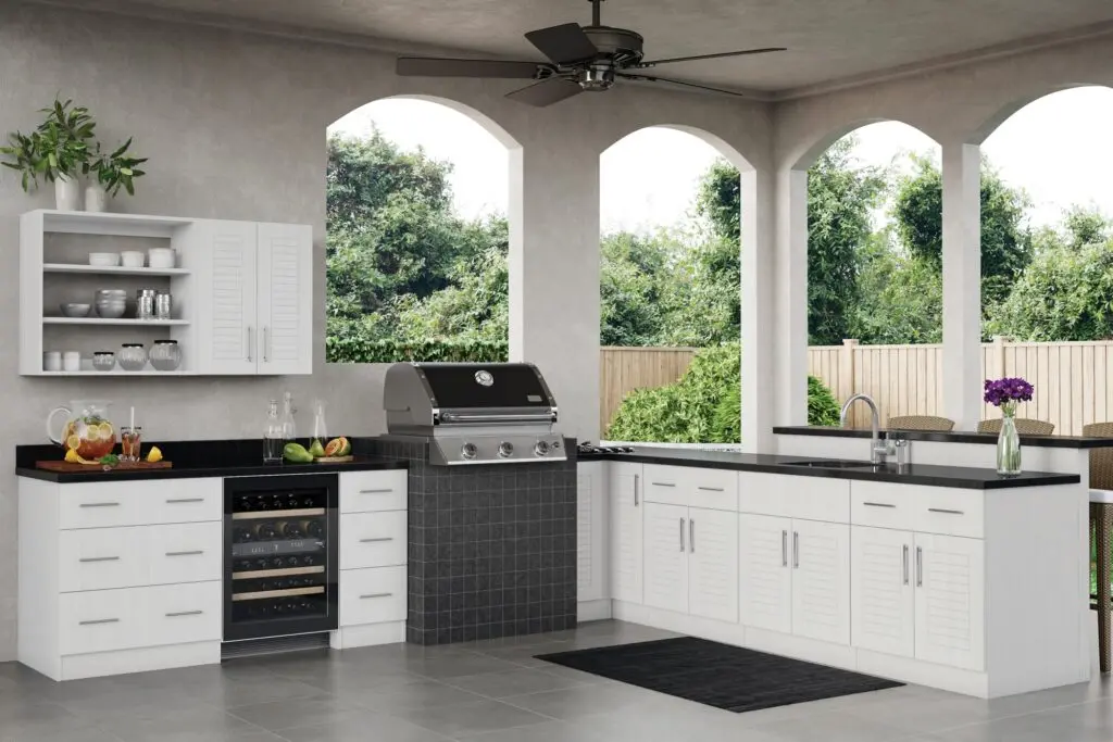 Kitchen and Bathroom Cabinets in a covered outdoor kitchen—white louvered cabinetry with stainless pulls, black countertops, built-in grill, beverage cooler, sink, and bar seating.