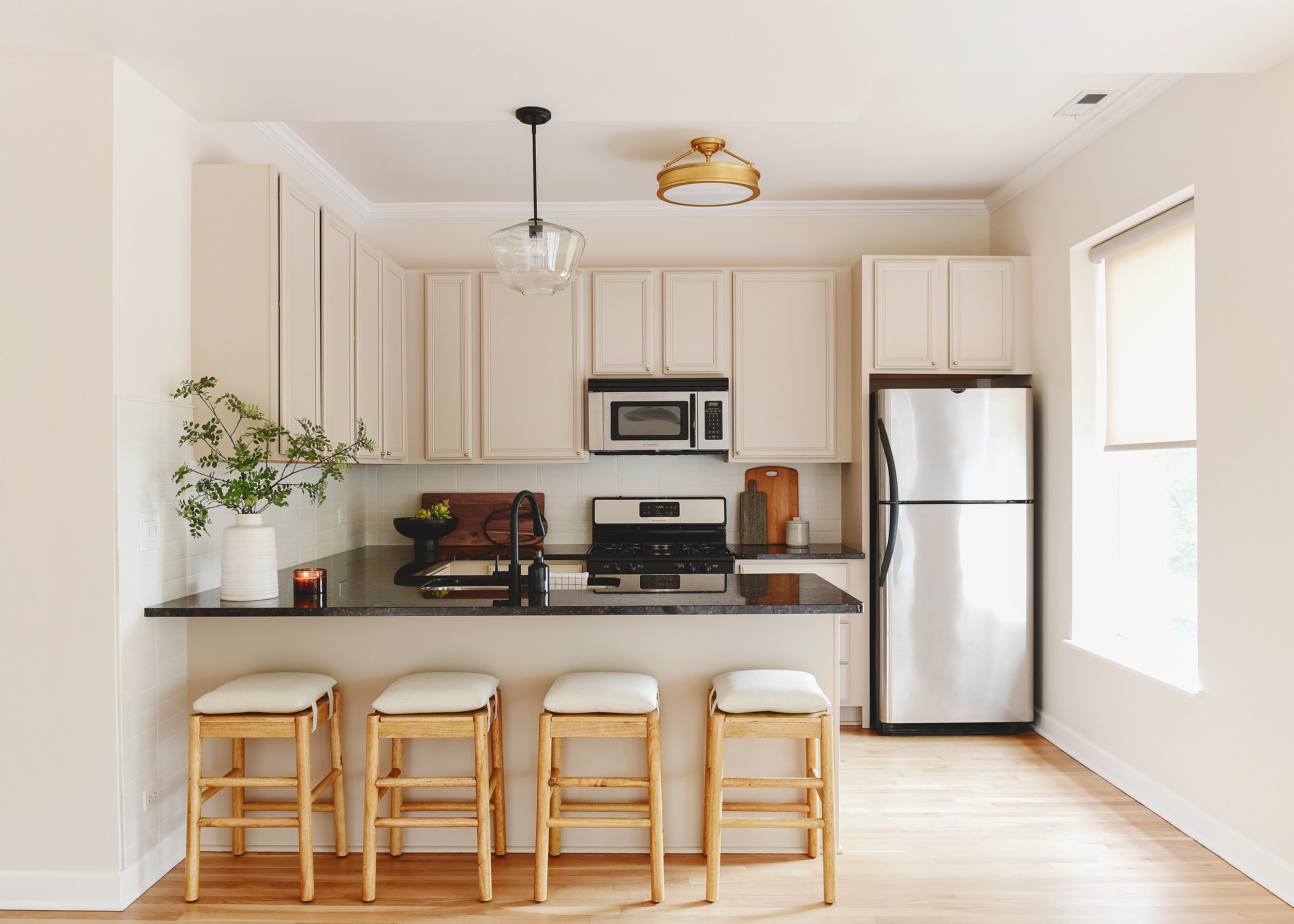 Condo kitchen with premium RTA cabinets Canada in soft beige, black quartz countertop, stainless appliances, and four wood stools.
