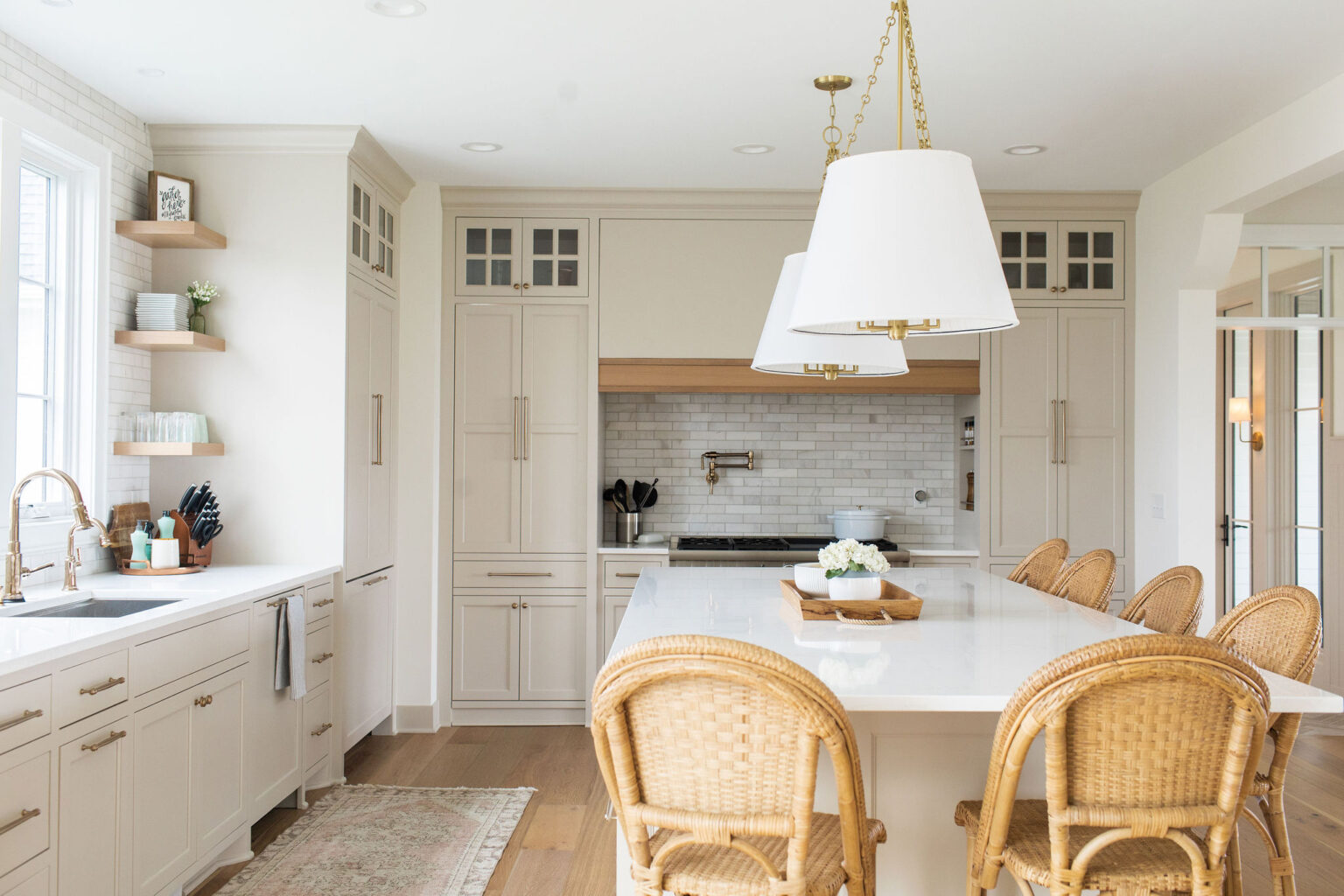 Bright Canadian kitchen with neutral cream shaker cabinets, brass hardware, white quartz island, and wicker bar stools for a timeless elegant look.