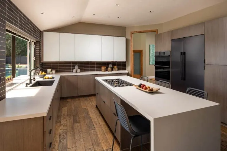 RTA cabinets in a modern kitchen with light wood bases, white uppers, tile backsplash, a large island cooktop, and matte-black fridge and ovens.