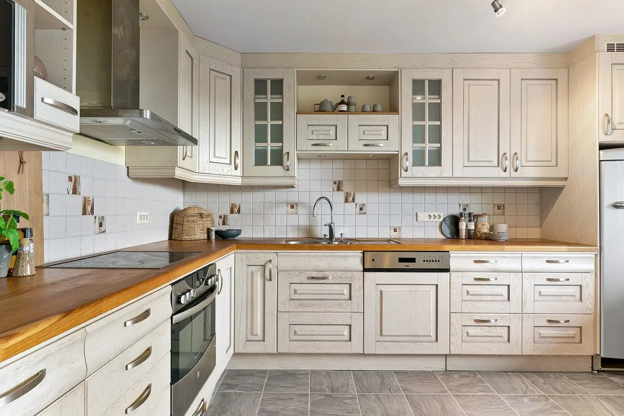 Light wood RTA cabinets in an L-shaped kitchen with glass-front uppers, wood countertops, tiled backsplash, and stainless range hood.