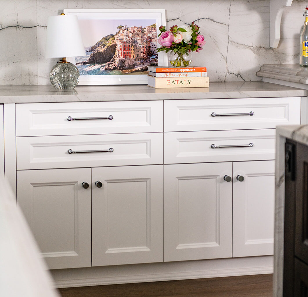 Clean white shaker RTA cabinets under a marble backsplash with polished hardware and a framed coastal print
