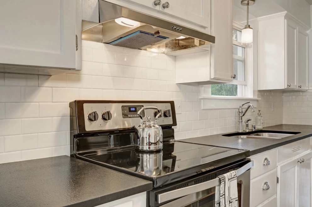 Electric range beneath a vent hood between white RTA cabinets and a subway-tile backsplash, illustrating appliance clearances