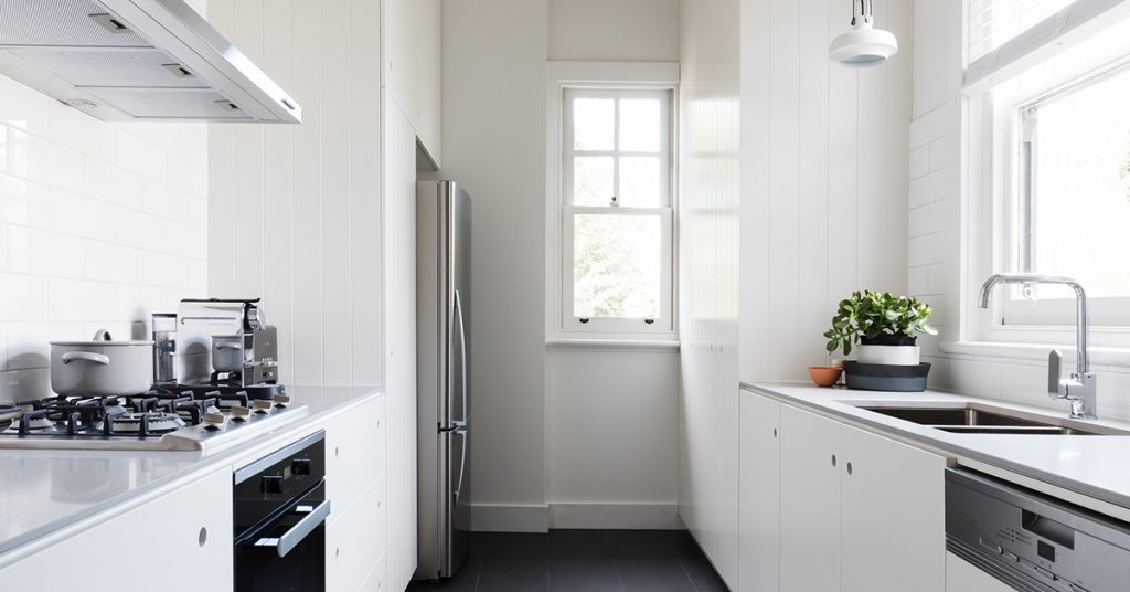 Bright galley kitchen with white flat-panel RTA cabinets, quartz countertops, gas cooktop, stainless fridge and dishwasher, and dark tile floor.
