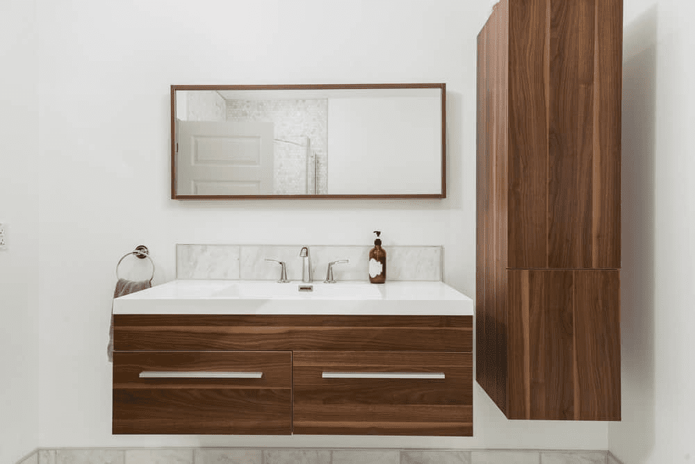 Bathroom cabinets — floating walnut vanity with integrated sink, long metal pulls, matching wall tower cabinet, frameless mirror, and white marble backsplash.