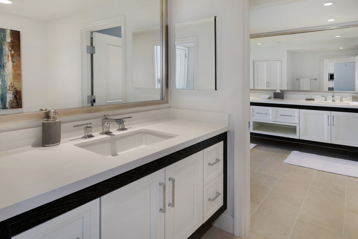 Contemporary bathroom with white shaker-style bathroom cabinets, sleek chrome handles, and quartz countertop with dual sinks and large mirrors.