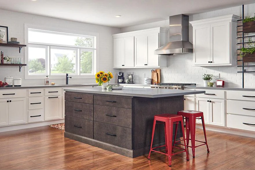RTA cabinets in a bright modern kitchen with white shaker doors, black pulls, a charcoal island, quartz counters, stainless hood, and red stools.