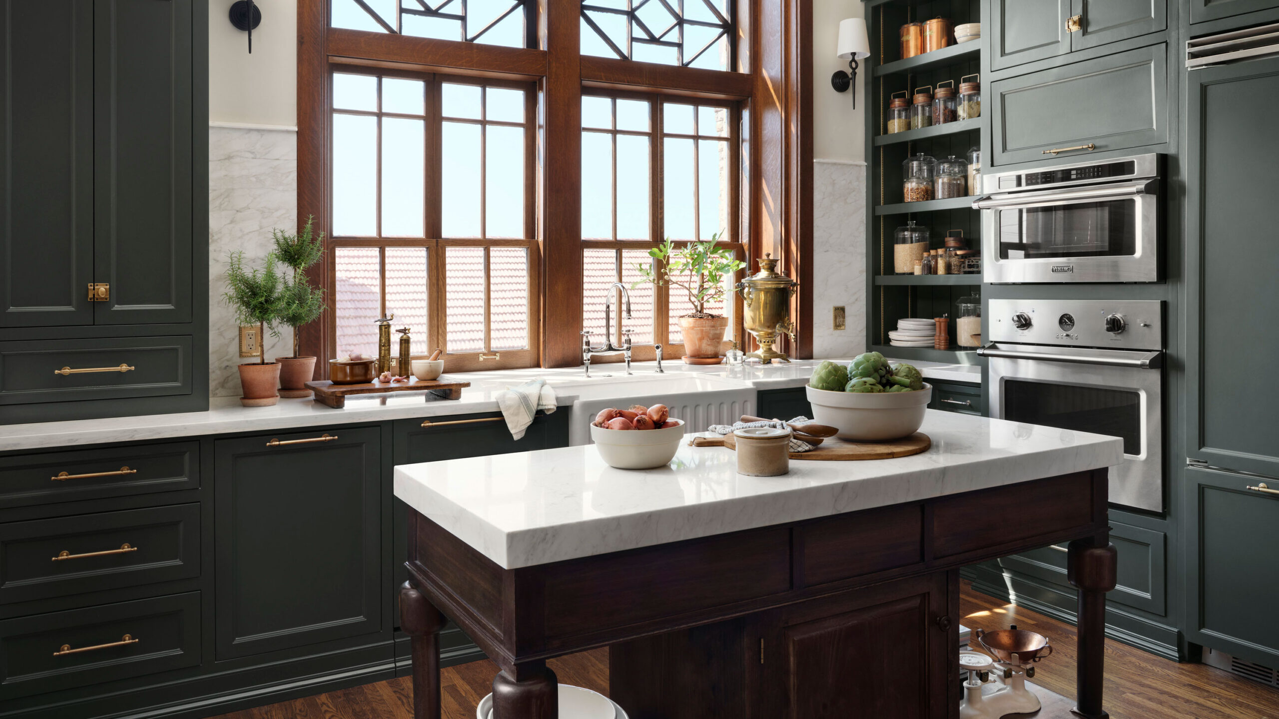 Luxury Canadian kitchen with deep forest-green shaker cabinets, brass hardware, white marble countertops, and natural wood accents — showcasing one of the best kitchen cabinet colors in Canada for 2025.