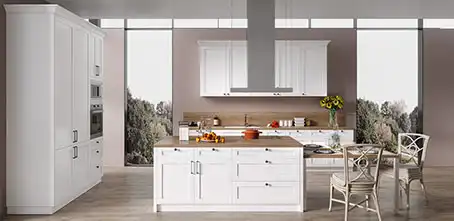 Open, airy kitchen with white Shaker RTA cabinets, wood-top island, stainless chimney hood, and built-in wall ovens in front of tall windows.