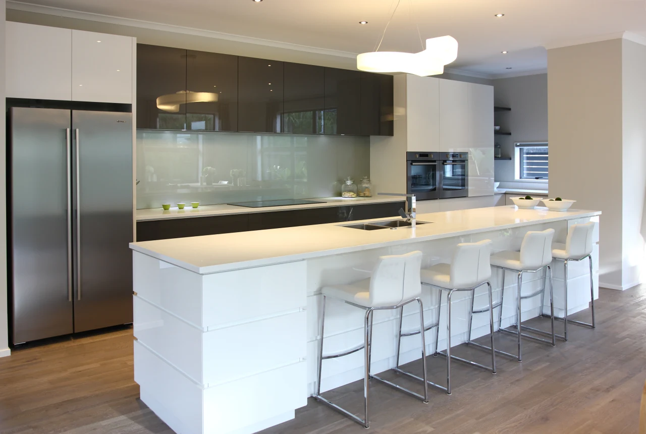 Modern open-plan kitchen with glossy white island, high-gloss kitchen cabinet fronts, stainless steel appliances, and white bar stools.