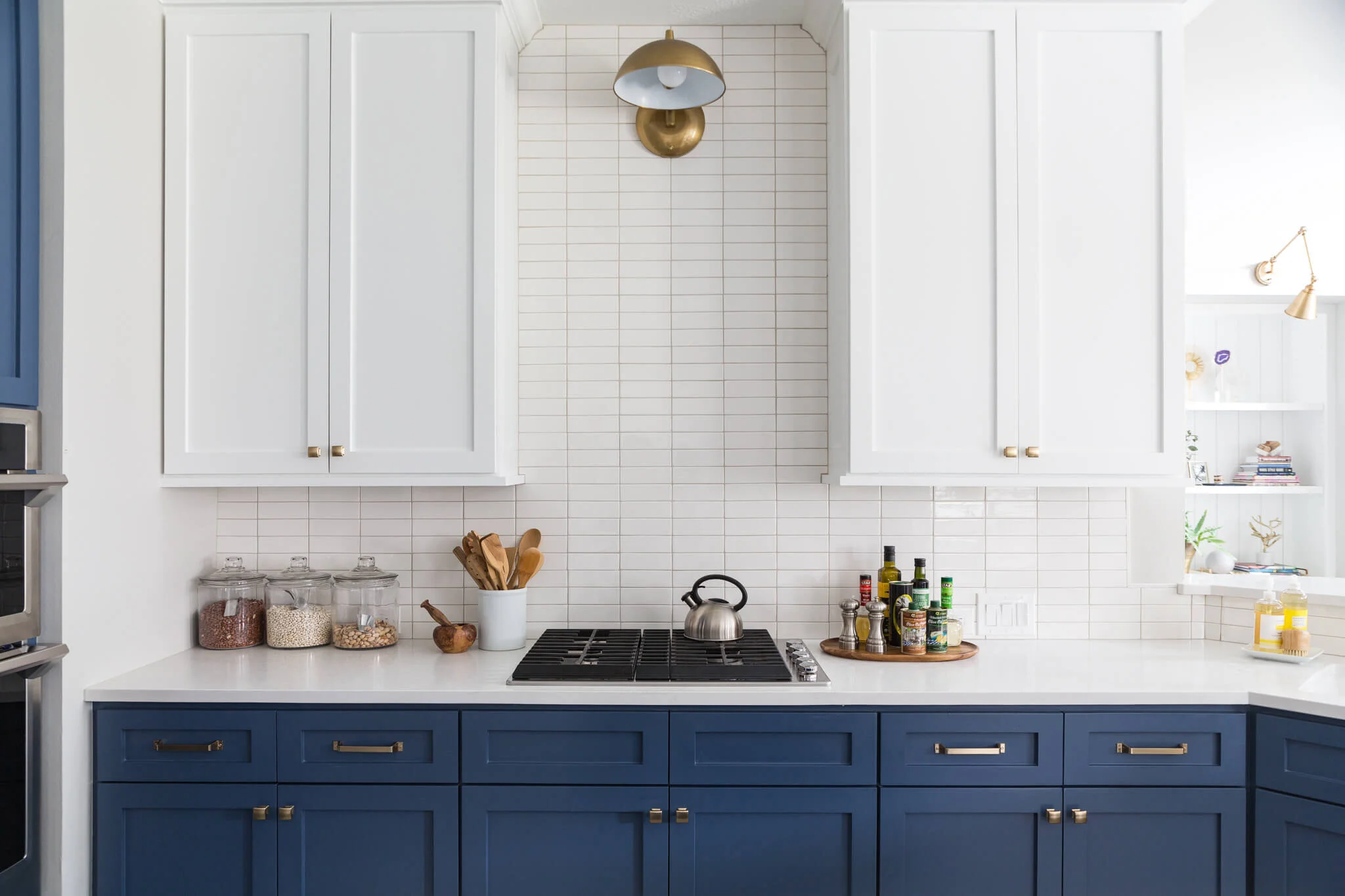 Two-tone kitchen cabinets in Canada: white Shaker uppers and navy base cabinets with brushed brass hardware, white tile backsplash, quartz countertop