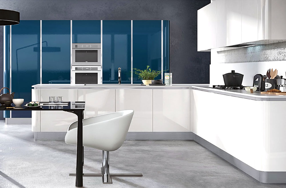 Modern glossy white kitchen cabinet set in a U-shaped layout with rounded corners, gray countertops, built-in ovens, blue glass accent wall, and a minimalist dining nook.