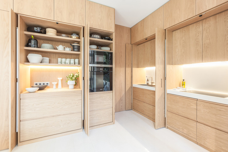 Minimal concealed kitchen cabinet in Canada with oak-veneer slab fronts, pocket doors, panel-ready appliances, and under-cabinet lighting