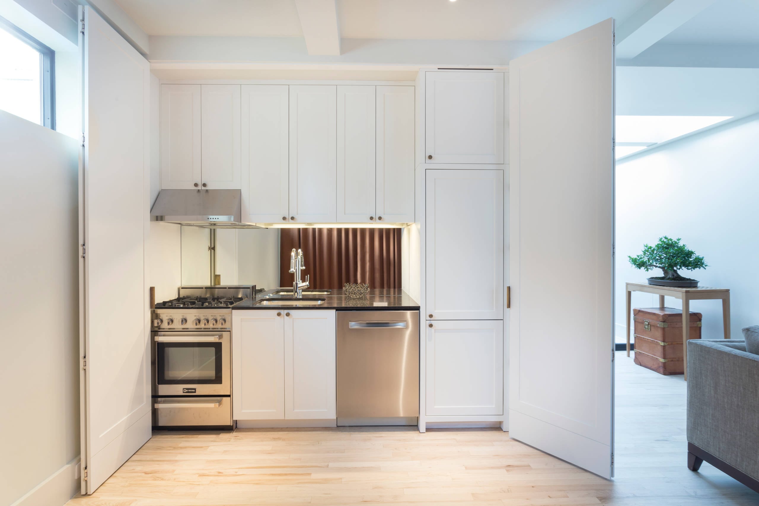 “Studio apartment kitchen in Canada with white shaker kitchen cabinet, tall pantry, and integrated appliances behind pocket doors