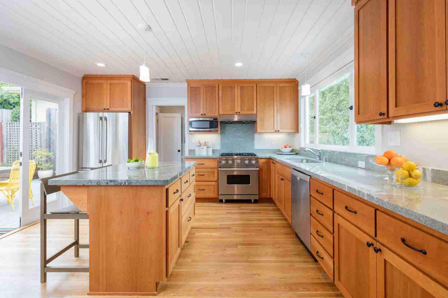 Bright, modern kitchen featuring warm wood kitchen cabinet design, stone countertops, stainless steel appliances, and a central island.