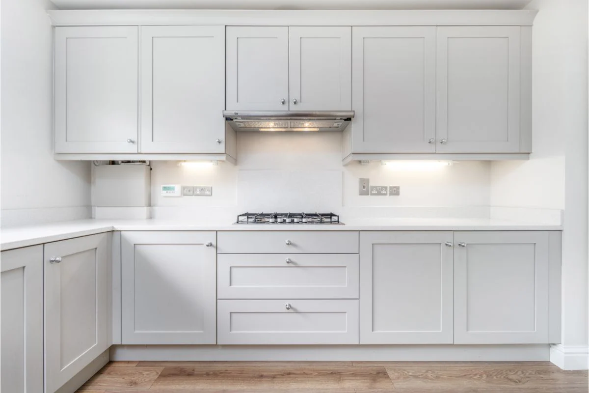 Modern light gray shaker kitchen cabinet design with white countertops, built-in gas cooktop and under-cabinet lighting in an L-shaped layout.