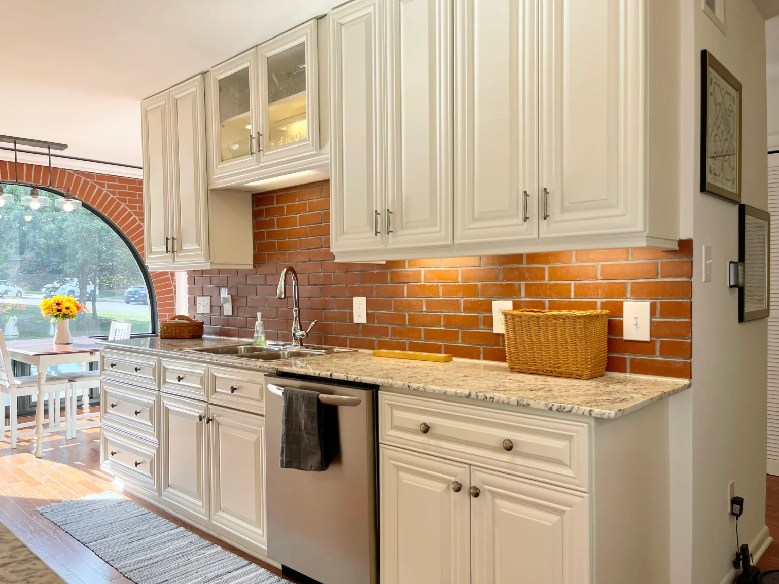 Premade kitchen cabinet installation with white raised-panel doors, brick backsplash, granite countertop, and stainless dishwasher.