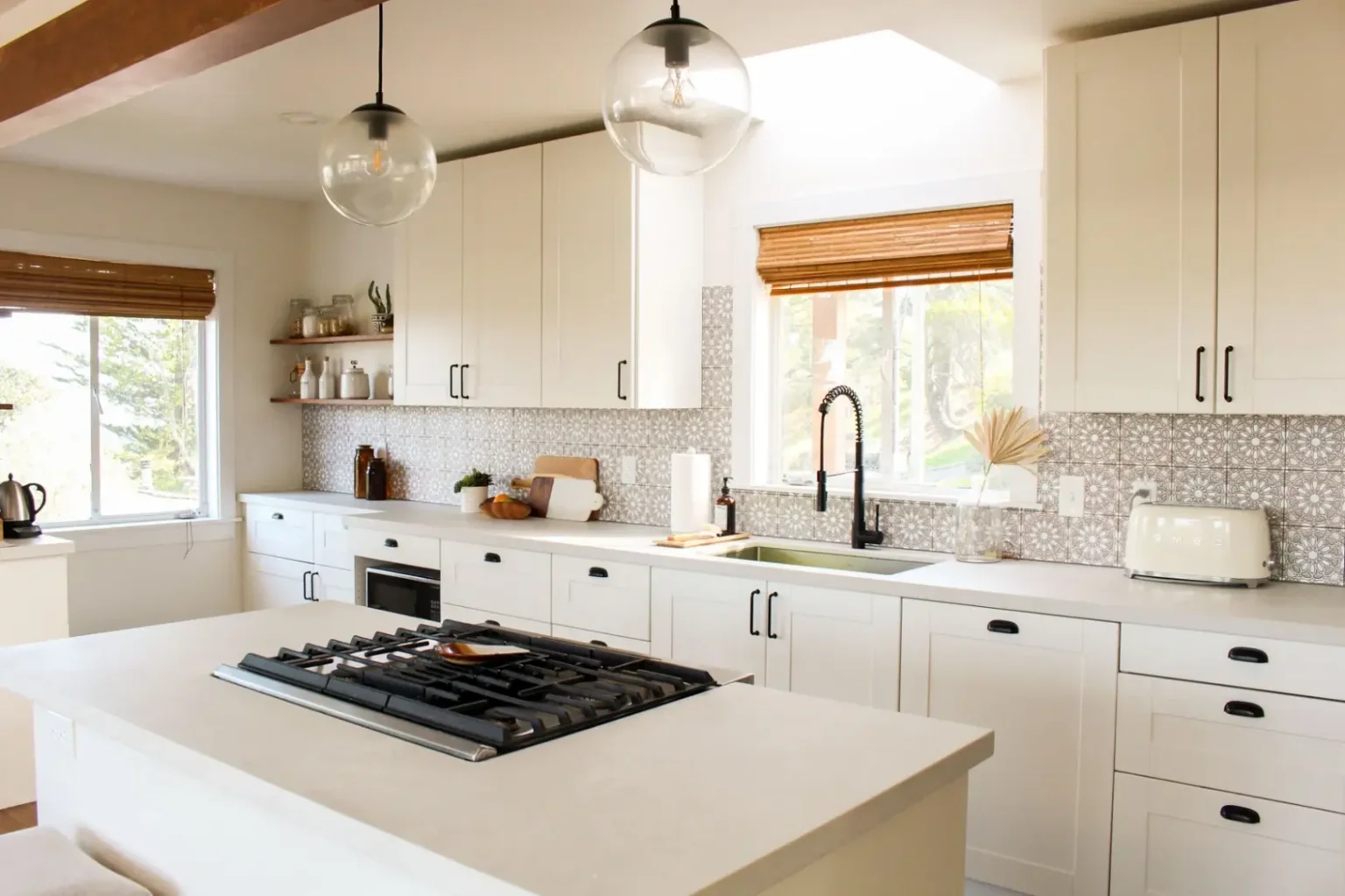 Bright modern kitchen with white Shaker flat pack kitchen cabinet doors, black handles, patterned tile backsplash, and a large island with a built-in gas cooktop.