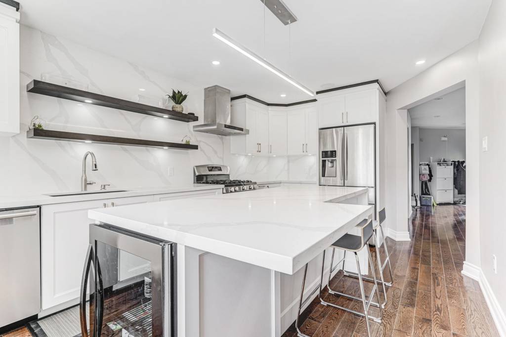 Modern white kitchen with flat-panel cabinets, oversized waterfall island, open floating shelves, and stainless appliances — Kitchen Cabinet Mississauga.
