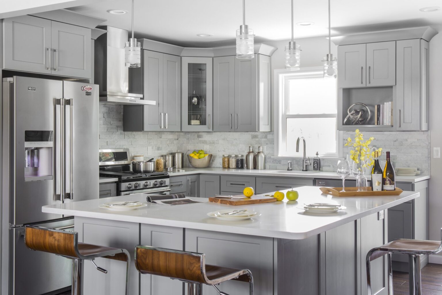 Modern kitchen with gray shaker cabinets, stainless steel appliances, marble-look backsplash, and a large white island with pendant lights—Kitchen Cabinet Mississauga.