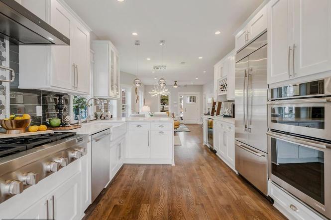 Kitchen Cabinet Mississauga in a bright galley kitchen with white shaker cabinets, stainless steel appliances, a large center island, recessed lighting, and warm hardwood floors.