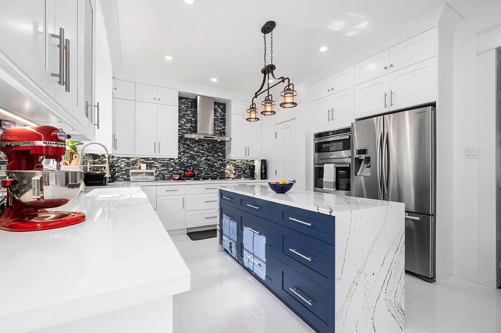 Modern white Kitchen cabinet Mississauga design with a navy-blue island, waterfall quartz countertop, and stainless steel appliances.
