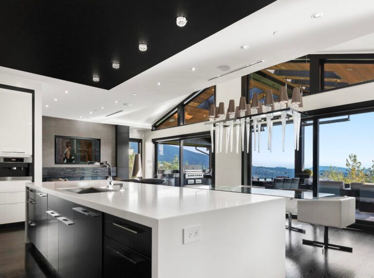 Ultra-modern open-concept kitchen with sleek black cabinets, large white waterfall island, statement chandelier, and floor-to-ceiling windows — Kitchen Cabinet Mississauga.