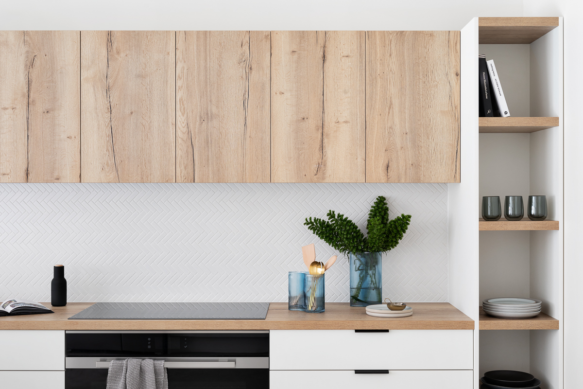 Modern kitchen with light oak flat pack kitchen cabinet uppers, white base drawers, wood countertop, and herringbone tile backsplash.