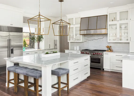 Kitchen cabinet design in a bright modern kitchen with white shaker cabinets, a large island with seating, brass pendant lights, and stainless steel range.