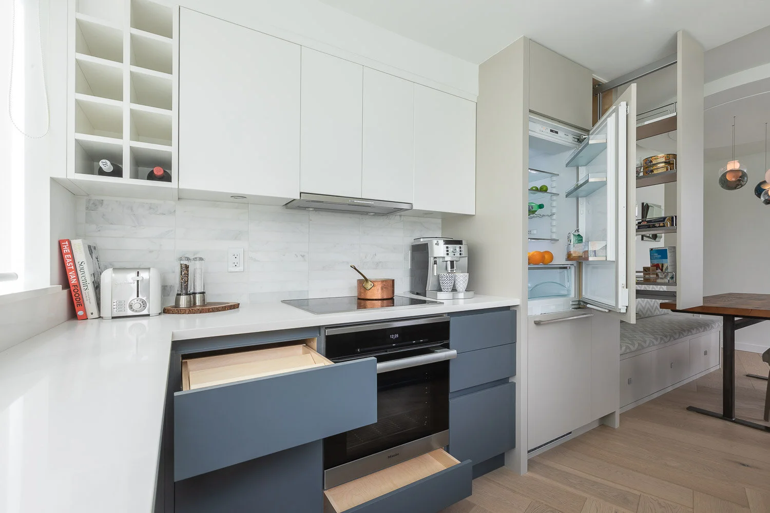 Modern condo kitchen with white upper cabinets, matte blue deep drawers, built-in oven, and an integrated fridge—smart storage design by Kitchen suppliers.