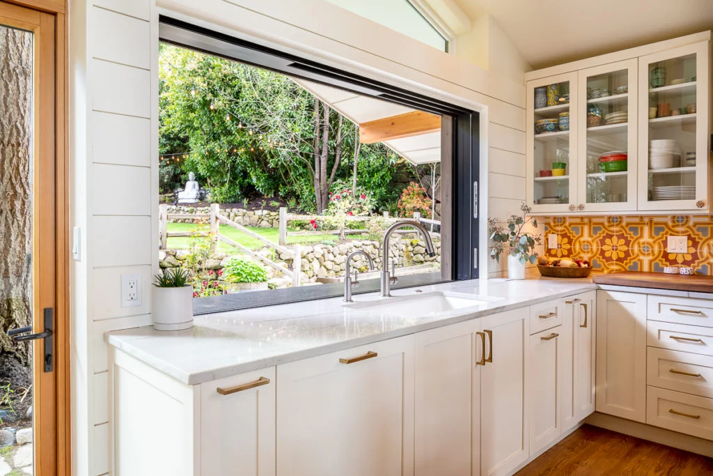 Bright white shaker Premade kitchen cabinet set with brass pulls, quartz countertop, and a large pass-through window over the sink.