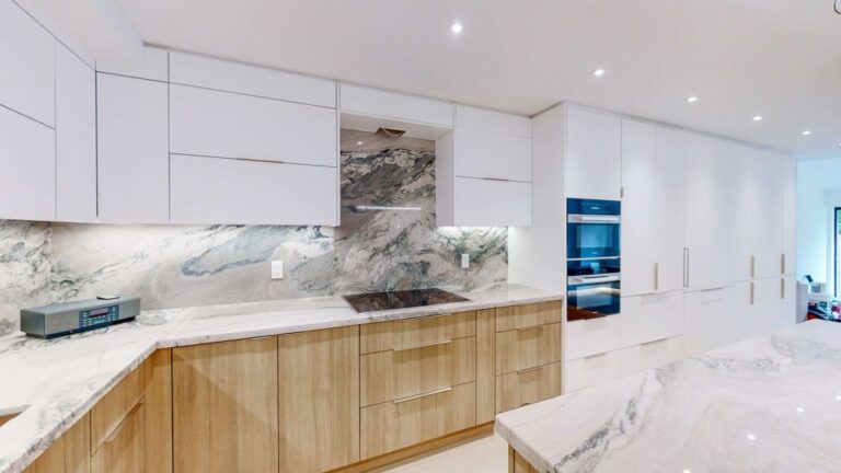 Modern condo kitchen designed by professional kitchen suppliers, featuring handleless white cabinets, wood-tone base units, marble backsplash, and integrated built-in appliances.