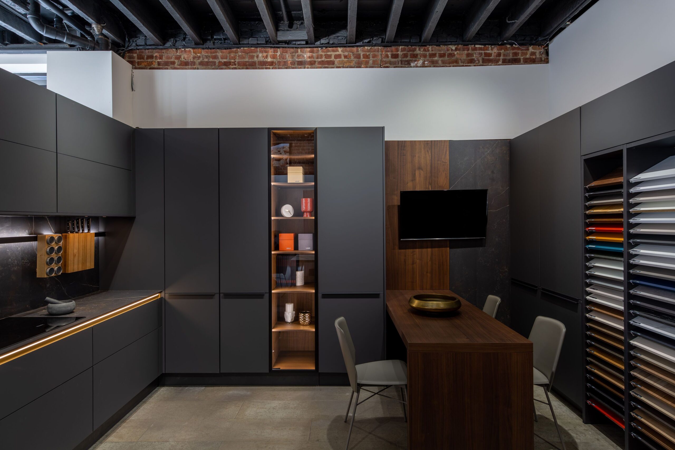 Modern kitchen showroom with matte black cabinets, wood island table, and finish sample wall—kitchen suppliers display for cabinet selection.