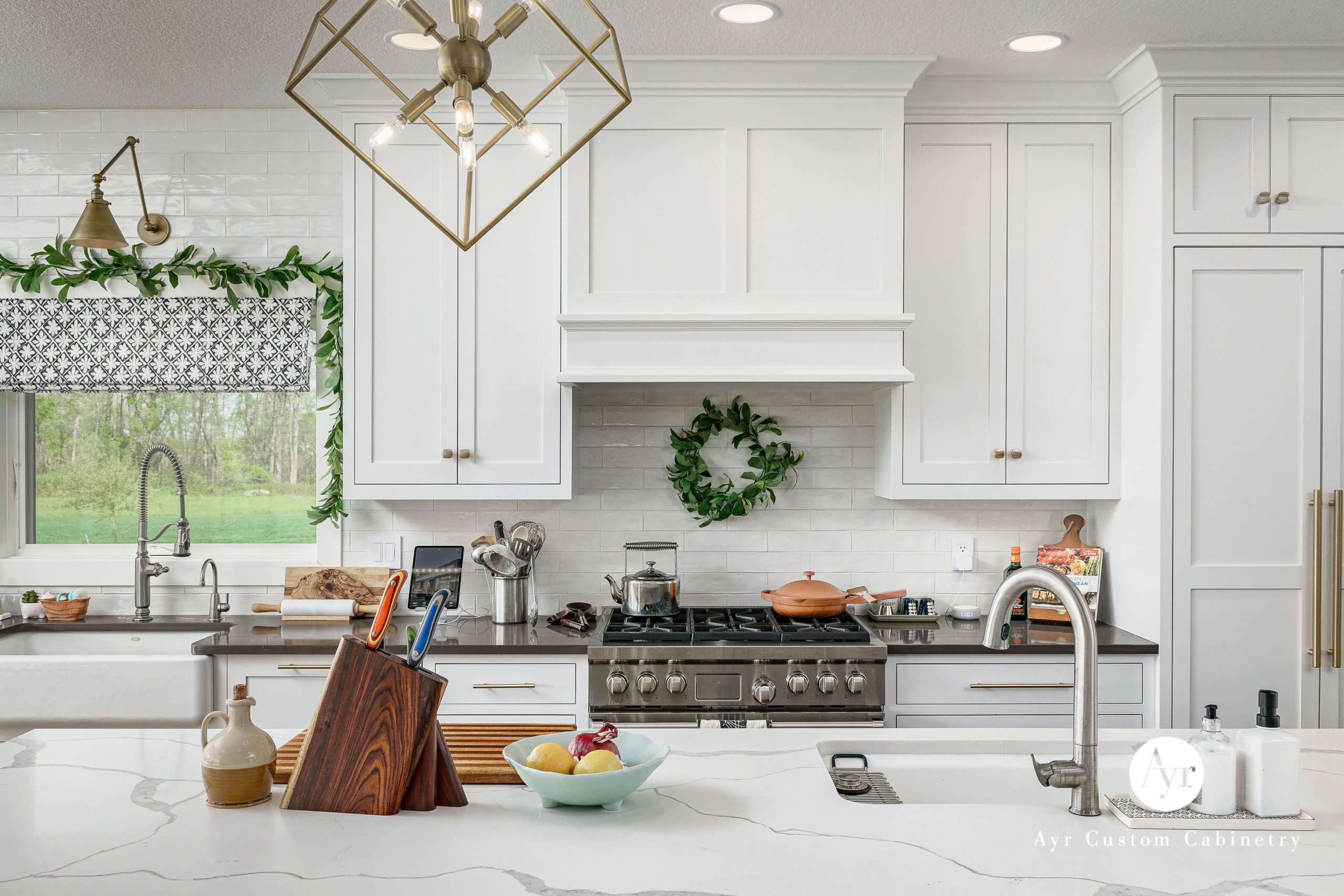 Modern white shaker kitchen with quartz island, brass hardware, farmhouse sink and gas range—quality cabinetry from trusted kitchen suppliers.