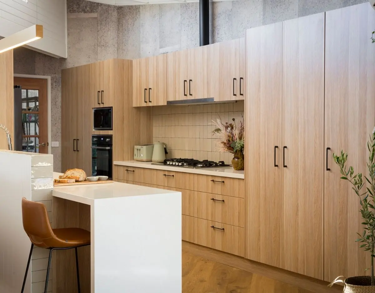 Modern light-wood Flat pack kitchen cabinet wall and pantry units with black handles, built-in oven, gas cooktop, and a white waterfall island in a minimalist kitchen.
