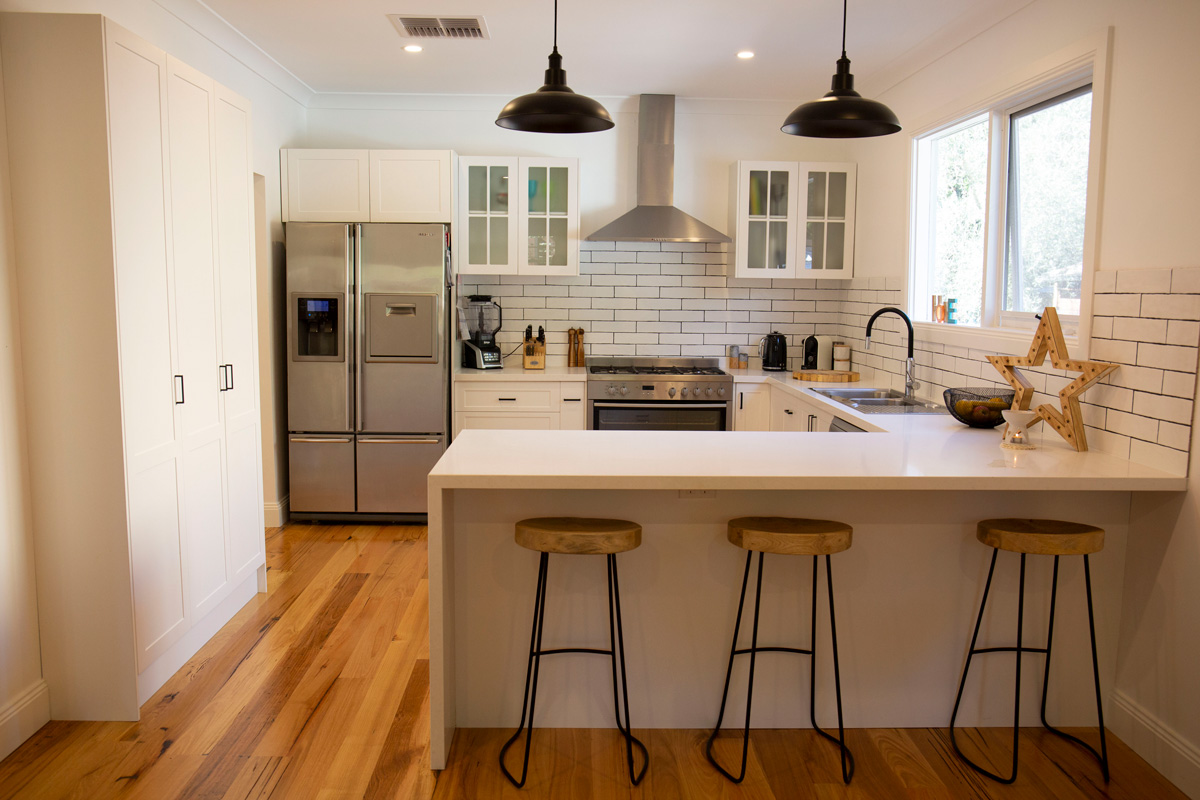 Flat pack kitchen cabinet in a modern white kitchen with shaker-style cabinets, plywood construction, large island seating, subway tile backsplash, and stainless steel appliances.