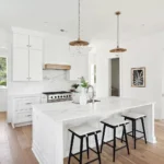 Bright modern white kitchen with large island, shaker cabinets, and marble countertops designed by professional kitchen suppliers