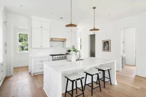 Bright modern white kitchen with large island, shaker cabinets, and marble countertops designed by professional kitchen suppliers
