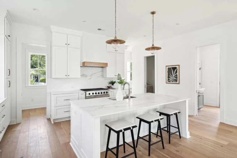 Bright modern white kitchen with large island, shaker cabinets, and marble countertops designed by professional kitchen suppliers