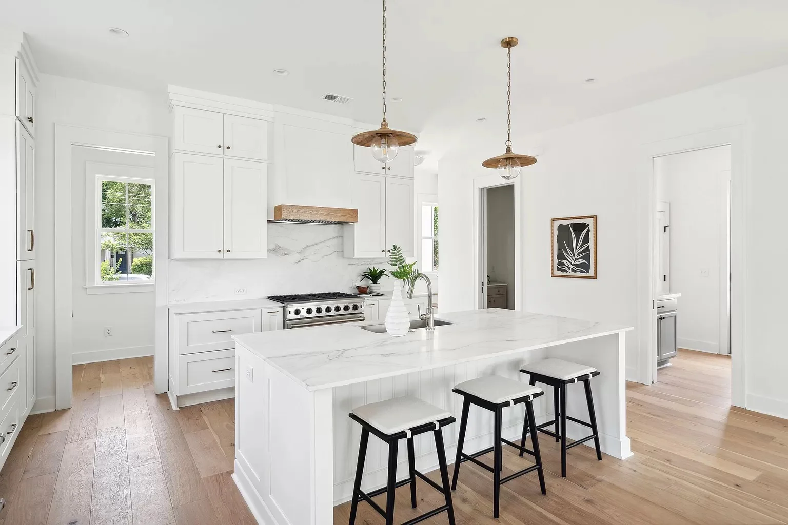 Bright modern white kitchen with large island, shaker cabinets, and marble countertops designed by professional kitchen suppliers