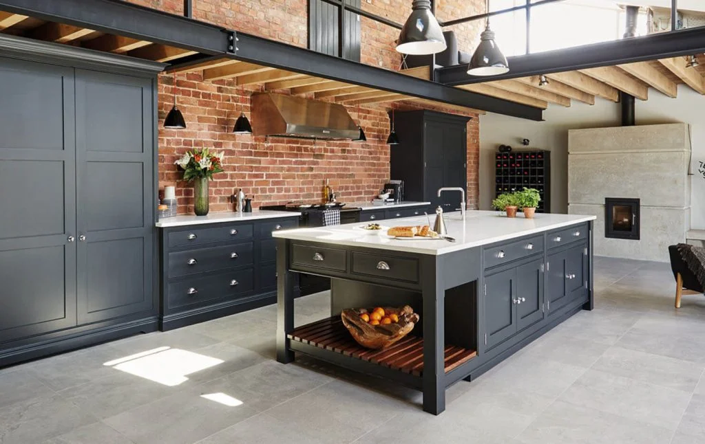 Kitchen suppliers inspiration: industrial loft kitchen with charcoal shaker cabinets, exposed brick wall, pendant lights, and a large island with a white countertop.