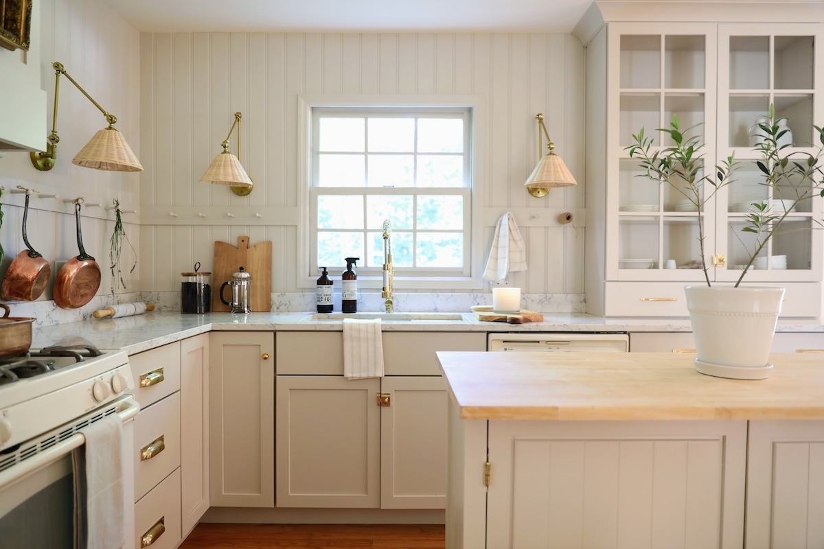 Bright modern farmhouse kitchen with white shaker cabinets, brass hardware, marble countertop, glass-front uppers, and a butcher-block island—design inspiration from a Kitchen cabinet supplier.